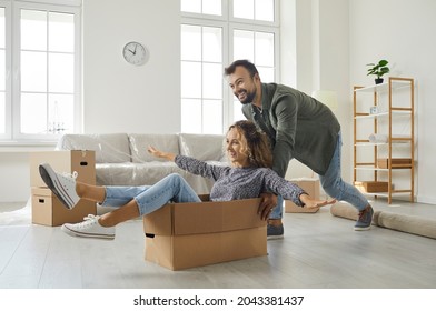 Happy Loving Young Couple Having Fun In New Home. Excited First Time Buyers Playing With Boxes In Modern Living Room Interior. Concept Of Real Estate, Mortgage, Buying House Or Apartment Of Your Dream