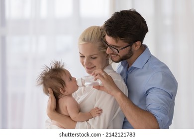 Happy loving young mom and dad caring of cute baby together, holding kid in arms, giving bottle with fresh water to drink, enjoying parenthood, family leisure time. Childcare, relationship concept - Powered by Shutterstock