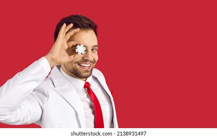 Happy Lucky Confident Handsome Young Man In Elegant White Suit And Tie Covering One Eye With Poker Chip In His Hand Standing On Red Blank Text Copyspace Studio Background. Casino And Gambling Concept