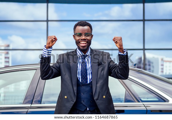 happy lucky and successful afro american\
businessman rejoices and enjoying success ahead of the car. concept\
of a good deal and\
victory