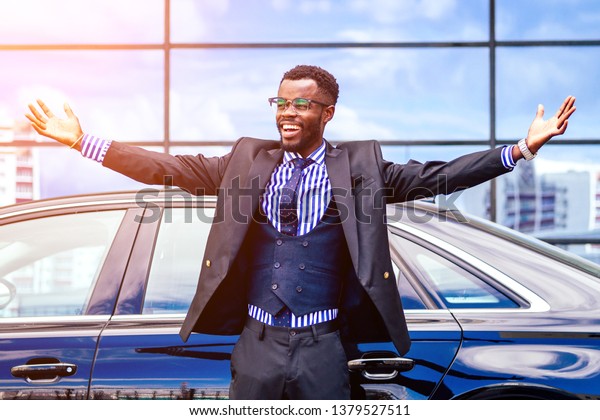 happy lucky and successful afro american\
businessman proud of himself and enjoying success ahead of the car.\
concept of a good deal and\
victory