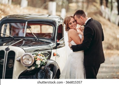 Happy luxury wedding couple kissing and embracing near retro with bouquet car in autumn