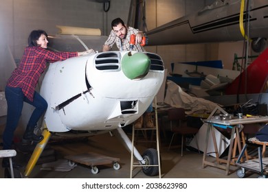 Happy Male Aircraft Enthusiast With Female Assistant Working In Workshop On Creating Of Light Aircraft Flying Model