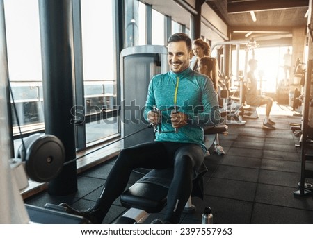 Happy male athlete doing rowing workout in the gym. Handsome man doing seated cable rows during fitness session in modern health center.