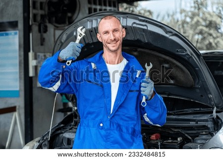 A happy male aut mechanic holding a wranch in each hands to celebrate while standing in front of a car with its hood open Stock fotó © 
