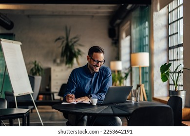 Happy male boss working online, making some notes, writing them with a pen. - Powered by Shutterstock