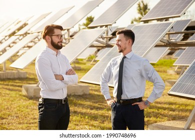 Happy Male Business Partners Discussing Energy Development Project While Standing Near Photovoltaic Panels On Green Solar Farm