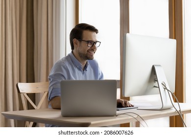 Happy male business professional leader working at workstation monitor and laptop computer on office table, looking at screen, smiling, laughing. Successful programmer, financial trader at workplace