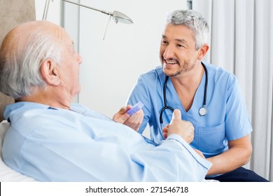 Happy Male Caretaker Discussing Prescription Medicine With Senior Man In Bedroom At Nursing Home