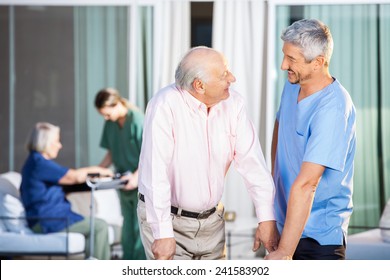 Happy Male Caretaker Looking At Disabled Senior Man At Nursing Home Yard