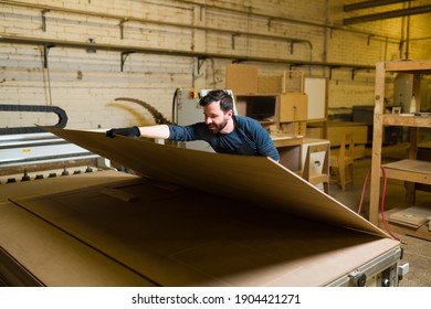 Happy male carpenter holding and lifting a plywood panel for a woodworking project. Male worker about to cut a wood sheet to build a piece of furniture