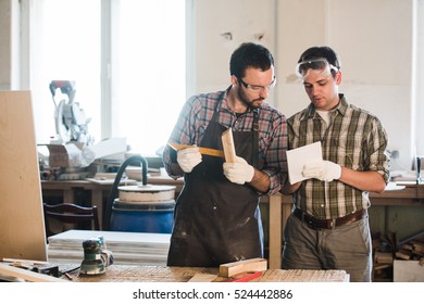 Happy male carpenter showing something to coworker at his notebook papers in workshop - Shutterstock ID 524442886