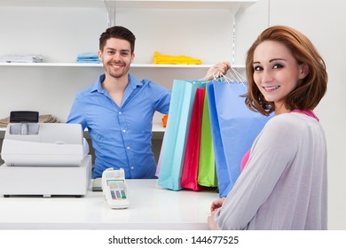 Happy Male Cashier Handing Over Shopping Bag To Customer