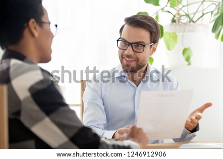 Happy male CEO or boss holding applicant resume talking with black female employee at interview, HR manager satisfied with candidate experience, African American girl make good first impression