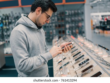 Happy Male Customer Choosing Smartphone In The Mobile Phone Shop. Difficult Decision. Various Choice. He Is Smiling