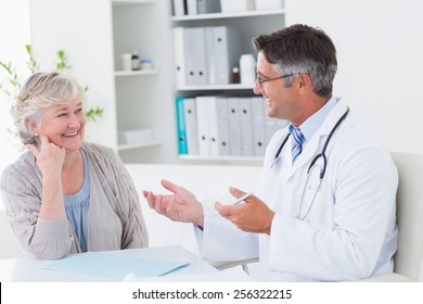 Happy male doctor discussing with senior patient at table in clinic