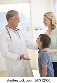 Happy Male Doctor Explaining Woman About Son's Health In Clinic