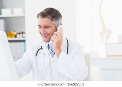 Happy Male Doctor Using Landline Phone In Clinic