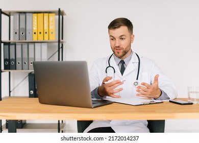 Happy Male Doctor Watching An Online Medical Webinar Or Training Seminar While Sitting With A Laptop In The Workplace.