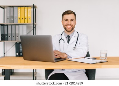 Happy Male Doctor Watching An Online Medical Webinar Or Training Seminar While Sitting With A Laptop In The Workplace.