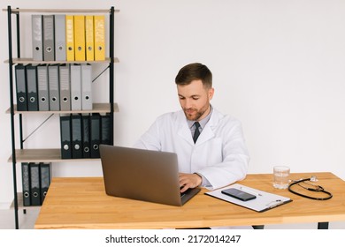 Happy Male Doctor Watching An Online Medical Webinar Or Training Seminar While Sitting With A Laptop In The Workplace.