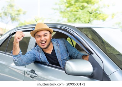 Happy male driver smiling while sitting in a car with open front window. Young asian man smile and looking through window enjoying trip. Man driving his car to travel on his holiday vacation time.