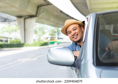 Happy Male Driver Smiling While Sitting In A Car With Open Front Window. Young Asian Man Smile And Looking Through Window. View Of A Young Man Driving His Car To Travel On His Holiday Vacation Time.