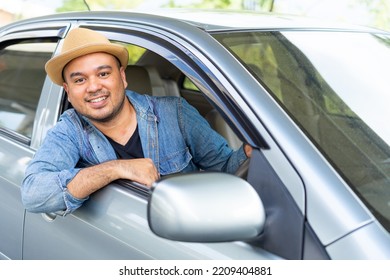 Happy Male Driver Smiling While Sitting In A Car With Open Front Window. Young Asian Man Smile And Looking Through Window. View Of A Young Man Driving His Car To Travel On His Holiday Vacation Time.