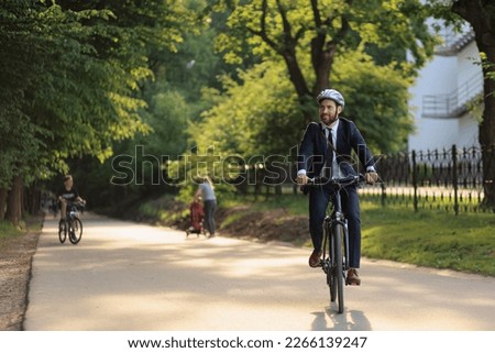 Happy male executive in business outfit returning from job on bicycle outdoor. Front view of determined office clerk feeling great, while cycling home from office in city park. Concept of transport.