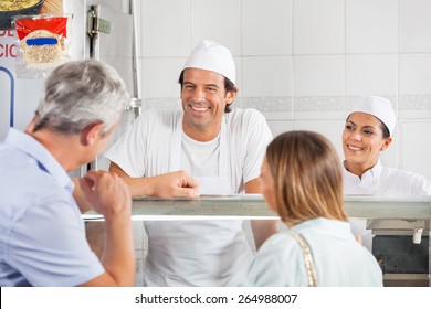 Happy male and female butchers looking at customer in shop - Powered by Shutterstock