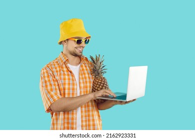 Happy male freelancer with laptop in hands working online during summer vacation. Smiling young man in summer beachwear with pineapple and laptop on light blue background. Banner. - Powered by Shutterstock