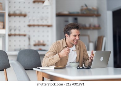 Happy Male Freelancer Talking To Someone During Video Call While Having Breakfast At Home Office.