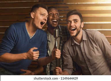 Happy male friends singing karaoke together in bar - Powered by Shutterstock