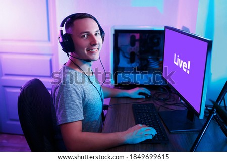 Happy male gamer enjoys playing computer games. Streamer studio with neon light. Cozy home environment. The man is having fun at the computer.