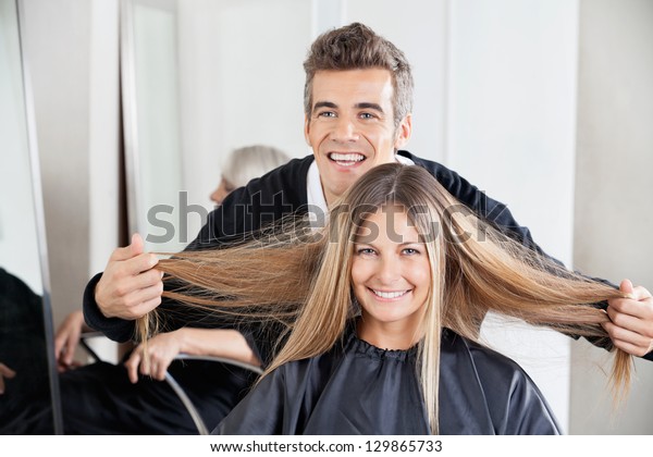 Happy Male Hairdresser Examining Female Customers Stock Photo