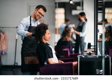 Happy male hairdresser styling hair of African American woman during appointment at the salon. Focus is on woman. - Shutterstock ID 2151717689