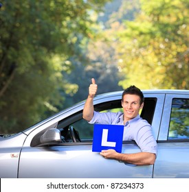 Happy male in his car holding a  L sign and giving thumb up after having his driver's licence