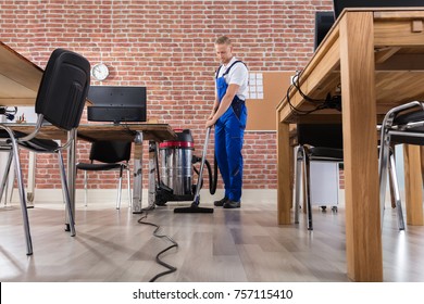 Happy Male Janitor Cleaning Floor With Vacuum Cleaner At Workplace