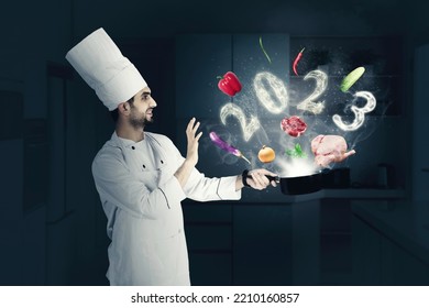 Happy male magician chef cooking on a saucepan with flying food ingredients and smoke shaped of 2023 numbers in the kitchen - Shutterstock ID 2210160857