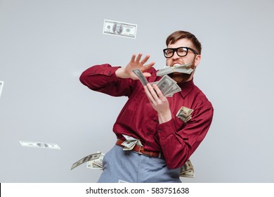 Happy Male nerd playing with money in studio. Isolated gray background