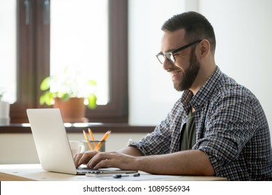 Happy male office worker smiling typing message at laptop, chatting with friends, writing positive email or consulting client online. Concept of laugher, positive work atmosphere, help and assistance - Shutterstock ID 1089556934