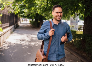 Happy male professional with digital tablet looking away. Young commuter wearing formals is carrying laptop bag. Entrepreneur is walking on sidewalk in city. - Powered by Shutterstock