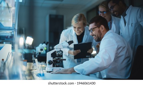 Happy Male Reseach Scientist Makes an Important Discovery While Researching Samples Under the Microscope. Happy Colleagues Congratulate it and Share Success with Fellow Bioengineers. - Shutterstock ID 1946061430