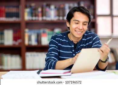 Happy male student at the library reading a book