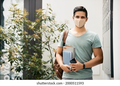 Happy Male Student Wearing Protective Face Mask At University Hallway And Looking At Camera. 