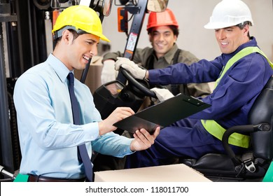 Happy Male Supervisor Communicating With Forklift Driver And Foreman At Warehouse