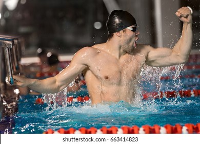 Happy male swimmer holding starting block at the edge of a pool and celebrating