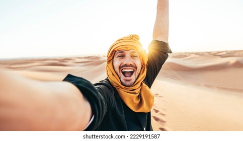 Happy male tourist taking selfie on sand dunes in the Africa desert, Sahara National Park - Influencer travel blogger enjoying trip while takes self portrait - Summer vacation and weekend activities
