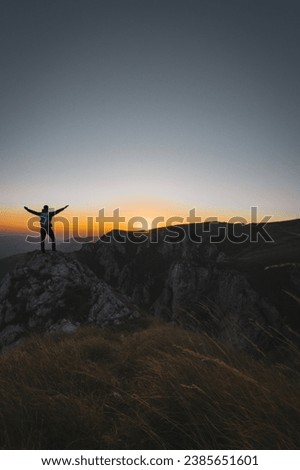 A happy male traveler celebrating a successful completed hiking route on the mountain top at sunset or sunrise adventure travel.