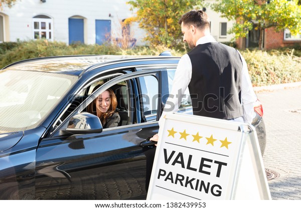 Happy\
Male Valet Opening Car Door Near Valet Parking\
Sign